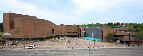 Modern architectural building with a curved facade and glass panels, surrounded by trees and a clear sky.
