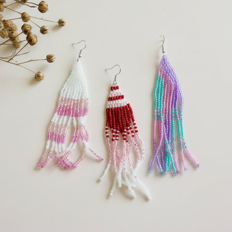 Three beaded earrings on a textured surface with dried flowers.